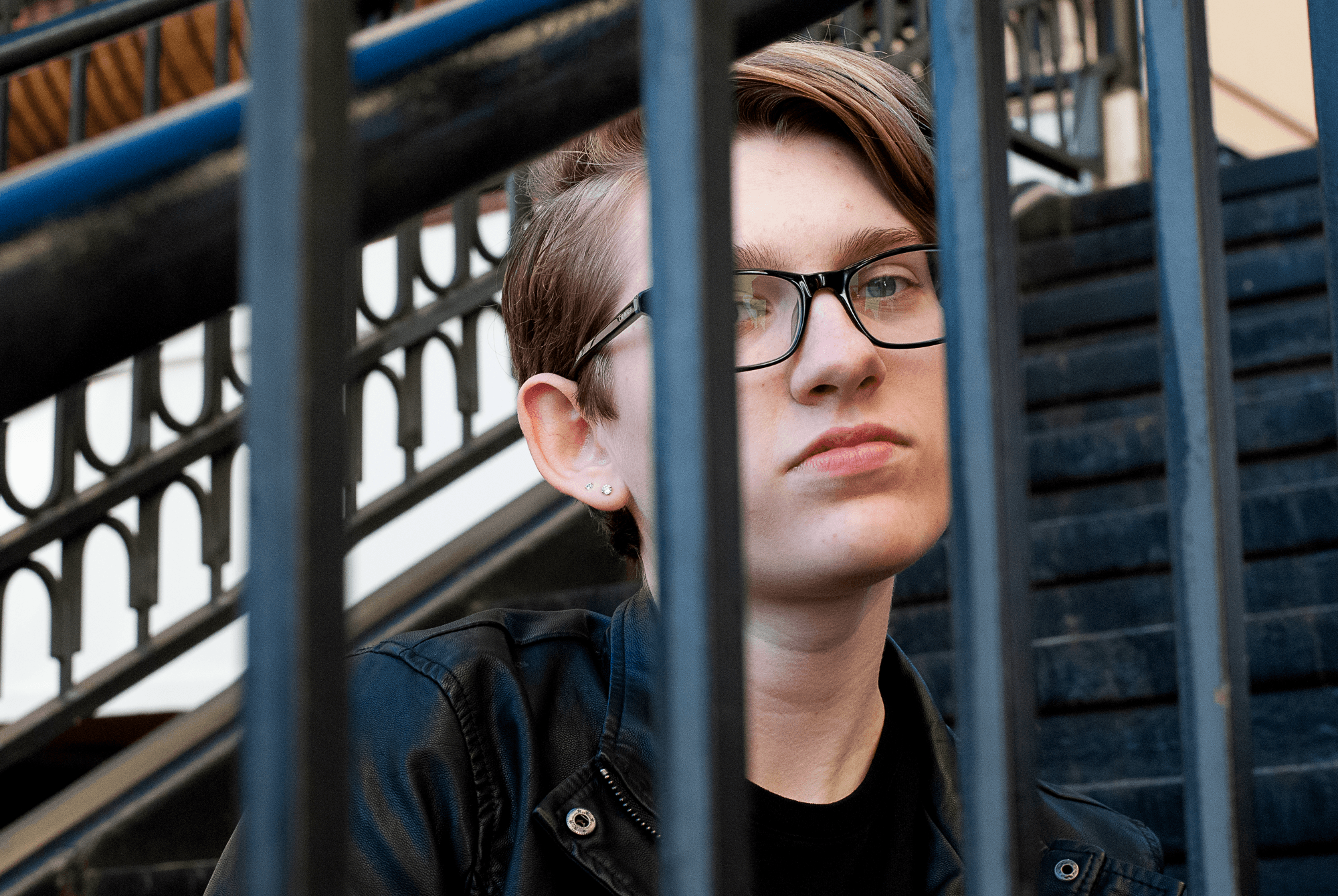 A portrait photograph of my friend looking at the camera with a serious expression through the bars of a staircase.