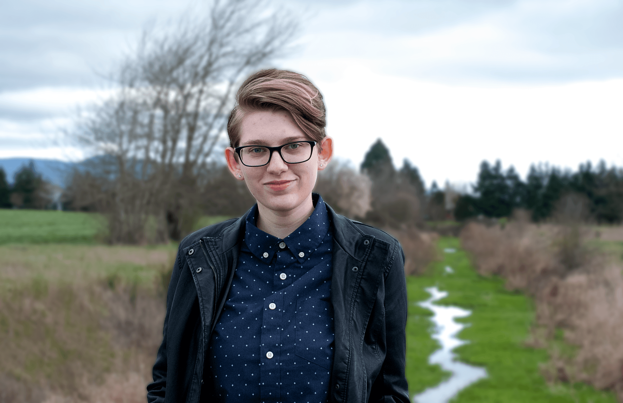 A portrait photograph of my friend standing on a bridge in front of stream.