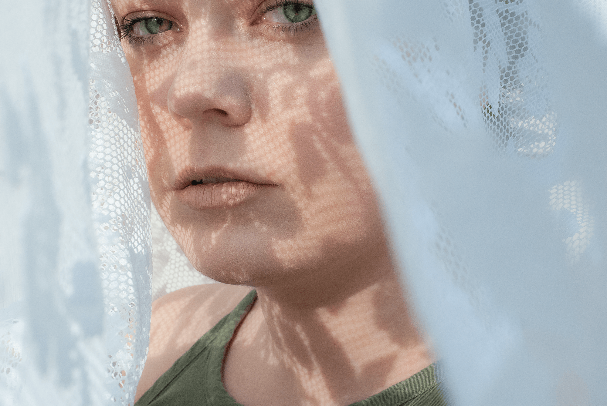 A photograph of me looking at the camera with the shadows of lace on my face.