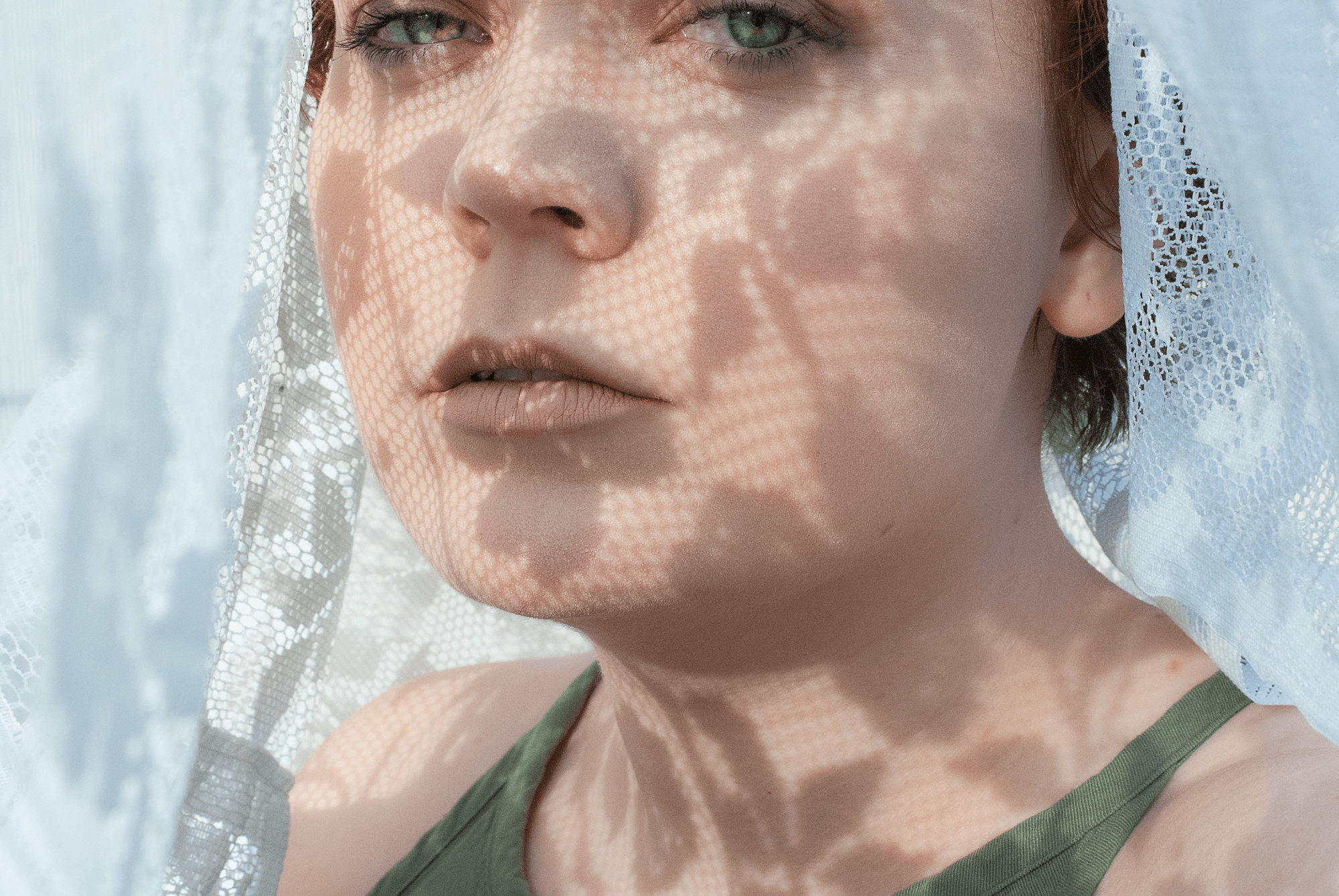 A photograph of me looking at the camera with the shadows of lace on my face.