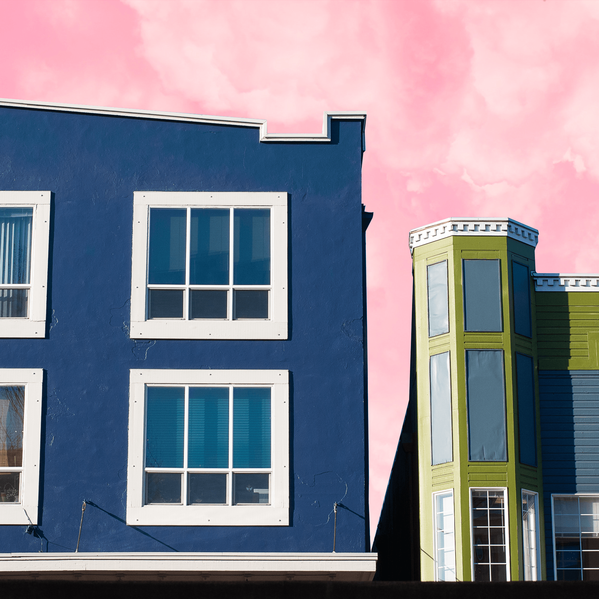 A photo of two colorful buildings with a sky of pink fluffy cotton candy skies behind them.