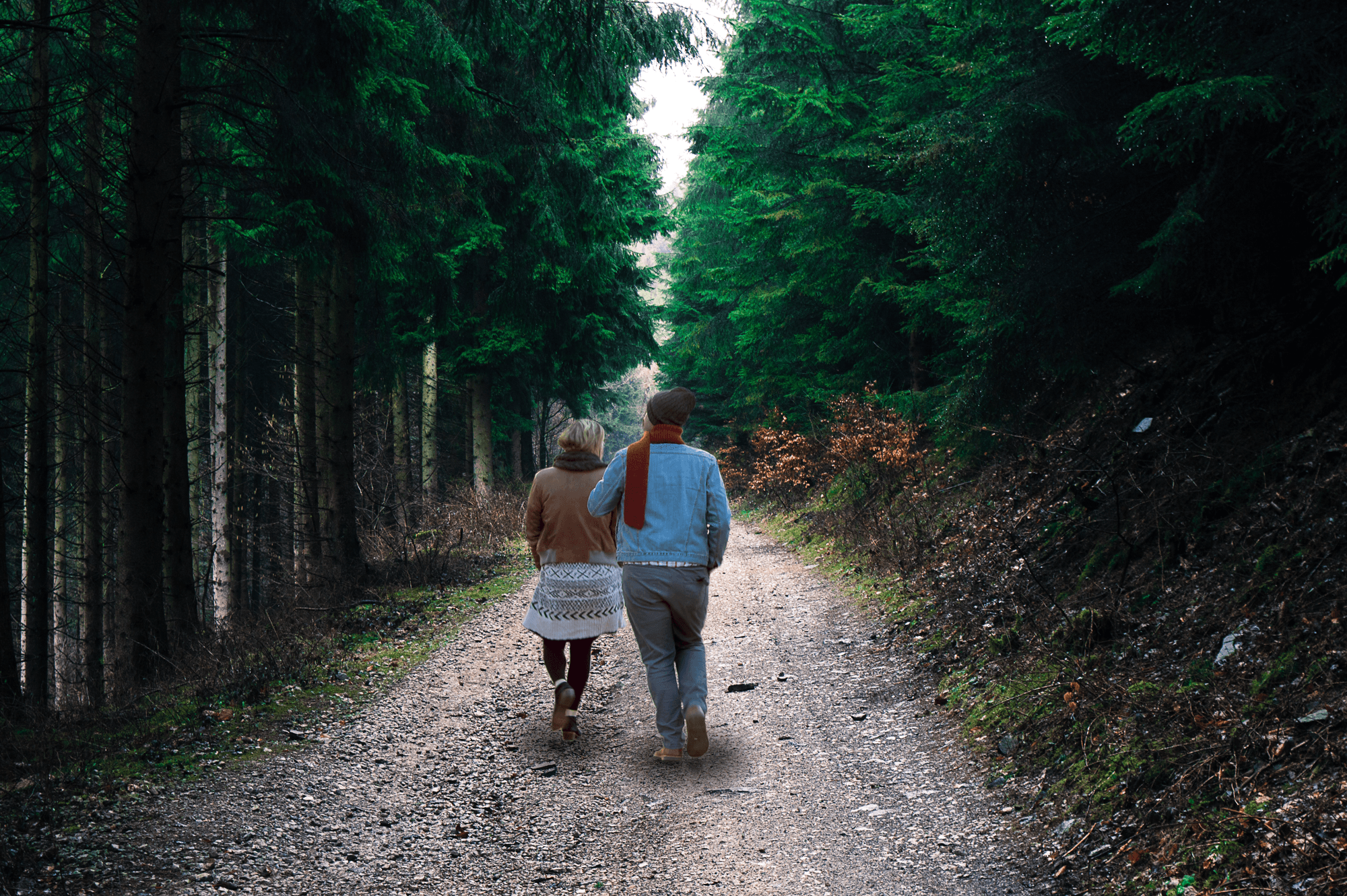 A photo of a man and woman walking down a path in the forest.